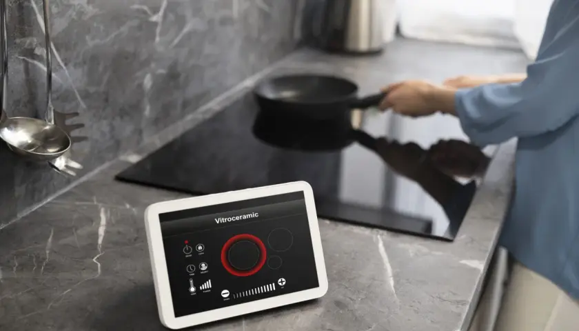 Cocina moderna con vitrocerámica y tablet para controlar electrodomésticos inteligentes. Una persona cocina en la placa de inducción.