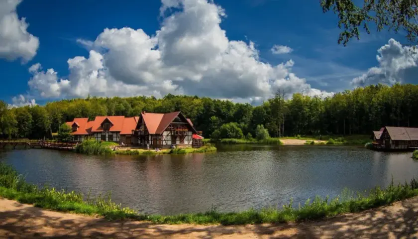 Idealne miejsce na długi weekend w sierpniu: urokliwe domki nad jeziorem, otoczone lasem, z pięknym niebem i chmurami.