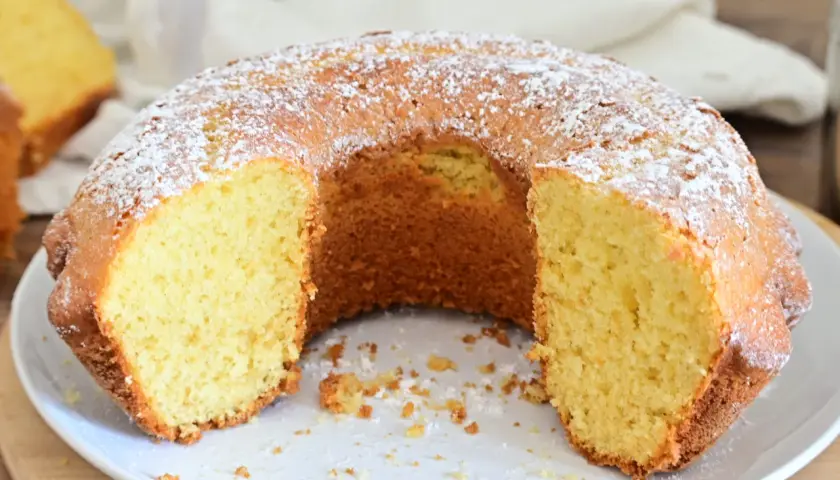 Una ciambella soffice, cosparsa di zucchero a velo, attende di essere gustata. La sua consistenza invitante promette un momento di puro piacere.