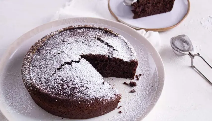 Gâteau au chocolat saupoudré de sucre glace, une part coupée. Idéal pour savoir par quoi remplacer le beurre dans un gâteau au chocolat.