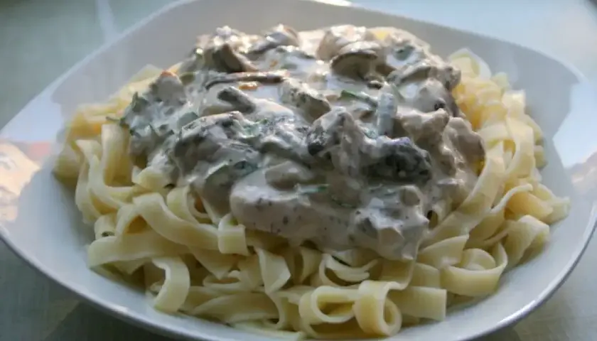 Pyszne tagliatelle z grzybami w kremowym sosie, podane na białym talerzu. Idealne danie dla miłośników grzybów.