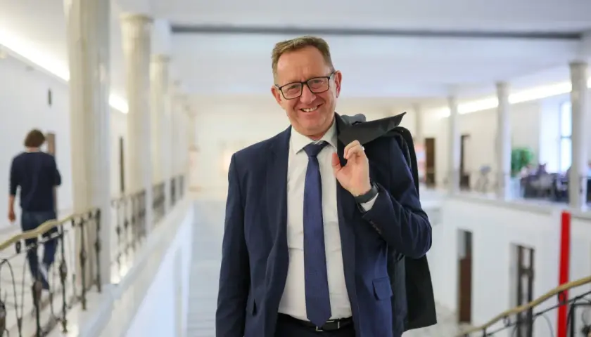 Uśmiechnięty mężczyzna w garniturze, który może być powiązany z pytaniem, dlaczego Robert Telus i Rafał Romanowski zostali zawieszeni w prawach członka.