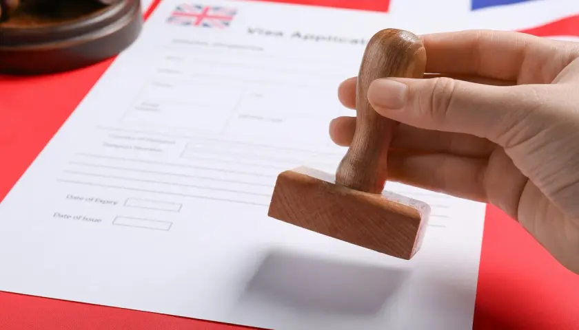 Dłoń trzyma pieczątkę nad formularzem wniosku o wizę do UK.