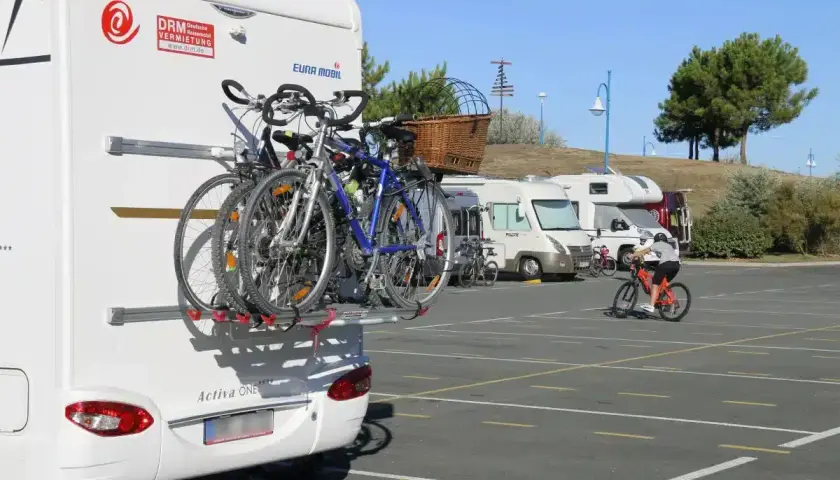 Camping-car avec vélos à l'arrière. Un cycliste s'entraîne sur un parking. Avis sur aire de camping-car.