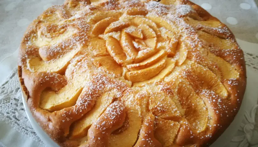Una deliziosa torta di mele senza glutine, decorata con fettine di mela a forma di rosa e spolverata di zucchero a velo.