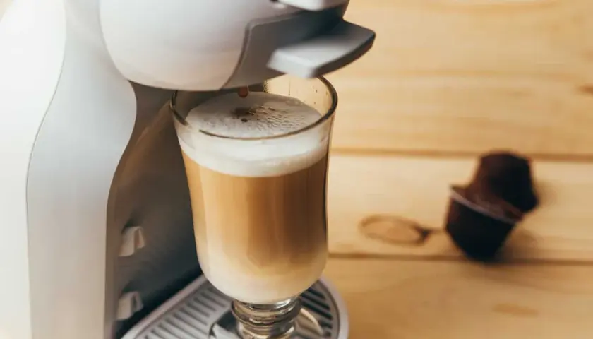Kawa w kapsułkach: czy jest zdrowa? Ekspres przygotowuje latte, obok leży kapsułka.