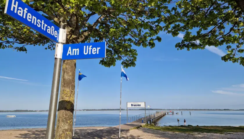 Schilder "Hafenstraße" und "Am Ufer" weisen den Weg zur **dranske strandpromenade**. Ein Steg führt ins ruhige Wasser.