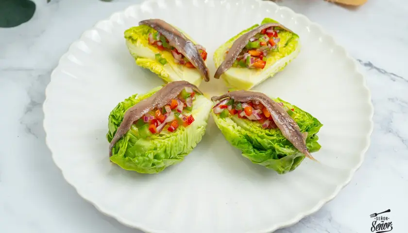 Cuatro cogollos de lechuga rellenos de pimientos y cebolla picados, coronados con anchoas. Un bocado fresco y sabroso.