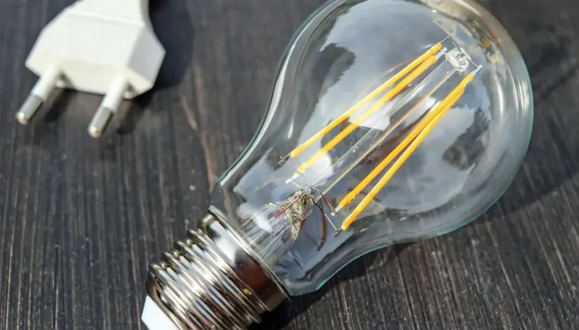 Żarówka LED i biała wtyczka na ciemnym drewnianym tle. Symbolizują potencjał, który czeka na aktywację, jak współczynnik jednoczesności w technologii.