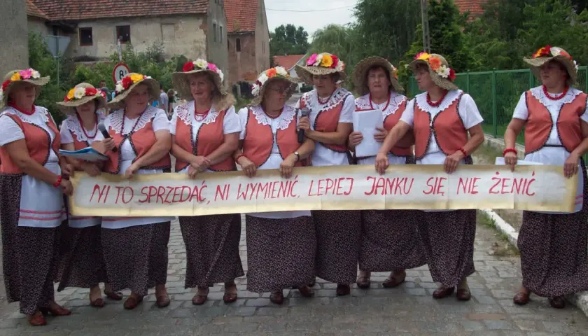 Kobiety w ludowych strojach trzymają transparent z napisem "Ni to sprzedać, ni wymienić, lepiej Janku się nie żenić" - śmieszne teksty na bramy weselne.