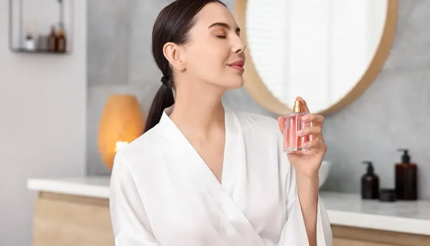 Kobieta w szlafroku rozpyla perfumy. Mgiełka od perfum różni się intensywnością zapachu i trwałością.