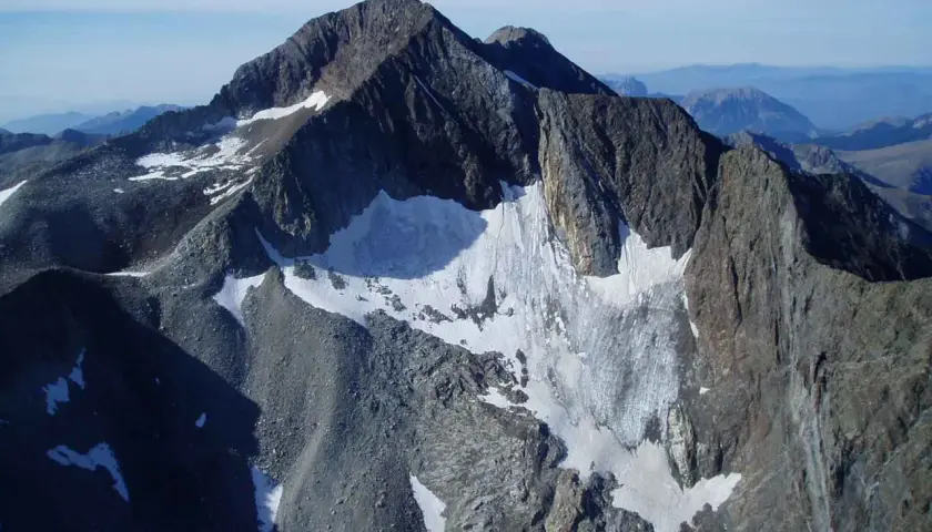 Majestuoso pico perdiguero cubierto de nieve y roca, con un glaciar que desciende por sus laderas.