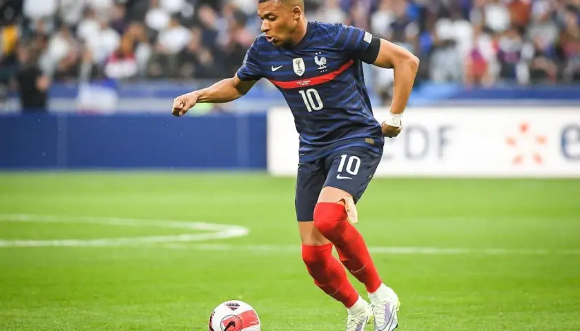 Kylian Mbappé w niebieskiej koszulce z numerem 10, w czerwonych getrach, wykonuje najszybszy sprint w piłce nożnej, prowadząc piłkę.