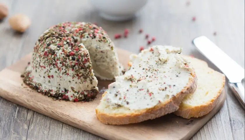 Queso vegano cubierto de pimienta y hierbas, servido en rebanadas de pan rústico.