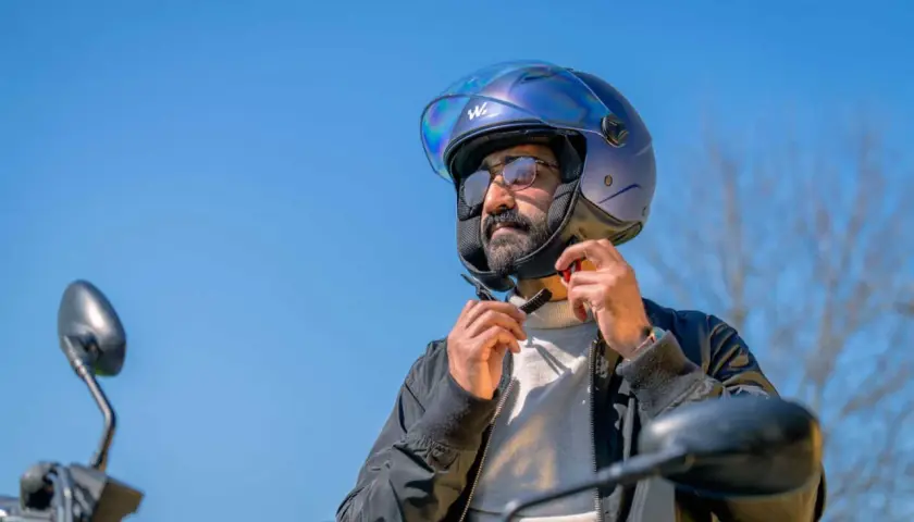 Uomo con casco blu metallizzato, pronto per un giro in moto. Il casco taglia 58 a cosa corrisponde? Probabilmente una misura media, perfetta per lui.