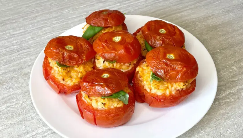 Sei pomodori ripieni di riso e basilico, cotti al forno, su un piatto bianco.