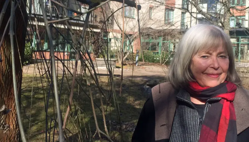 Agneta Pleijel ung, med grått hår och röd halsduk, ler mot kameran i en trädgård.