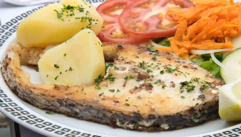 Un succulento pesce spada al forno, servito con patate bollite, pomodori a fette, carote grattugiate e insalata fresca.