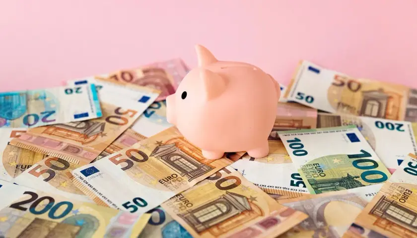 Różowa świnka-skarbonka na stosie banknotów euro. Zastanawiasz się nad oprocentowaniem konta walutowego?