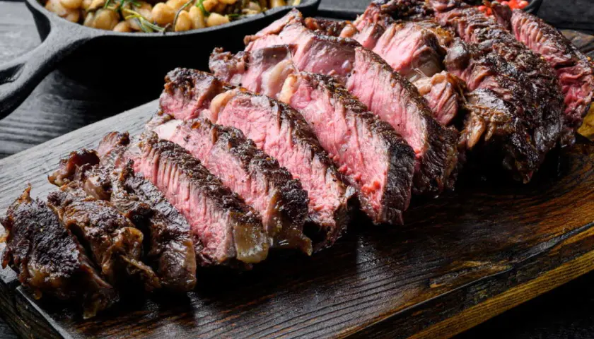 Côte de bœuf juteuse, tranchée et prête à être dégustée. Parfaitement cuite sur la plancha, accompagnée de haricots et de poivre rose.