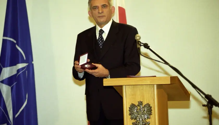 Jerzy Buzek, premier Polski, prezentuje medal. Obok flagi NATO i Polski.