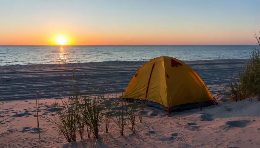 Żółty namiot na piaszczystej plaży, z widokiem na spokojne morze i zachodzące słońce. Idealne miejsce na nocleg, gdzie pole namiotowe nad morzem wita o poranku.