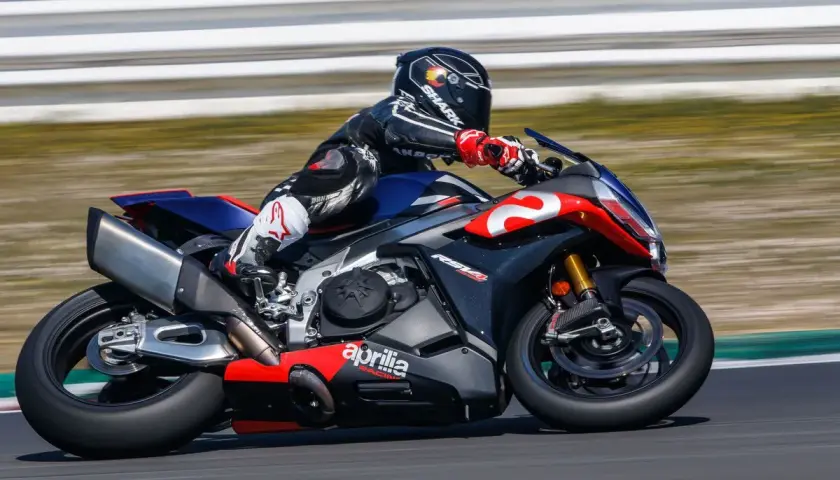 Piloto en una Aprilia RSV4 1100 en circuito, con traje de cuero negro y rojo, casco Shark.