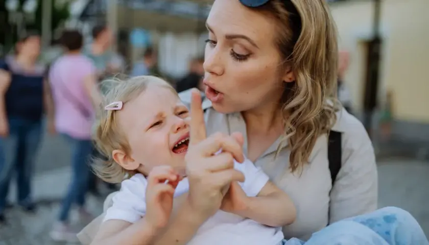 Bambina piange mentre la madre, forse afflitta da depressione, cerca di calmarla. Gli effetti della madre depressa sui figli adulti sono complessi.