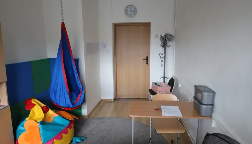 Przytulny gabinet pedagoga szkolnego z kolorowym workiem sako w kształcie ptaka, huśtawką i biurkiem.