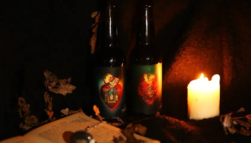 Deux bouteilles de bière la débauche 27 degré, éclairées par une bougie, entourées de feuilles mortes et d'un livre ouvert.