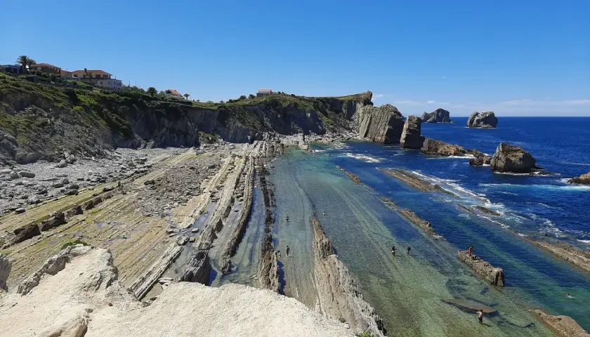 Espectacular vista de la playa de Arnia con sus formaciones rocosas y aguas cristalinas. Personas disfrutan del mar.