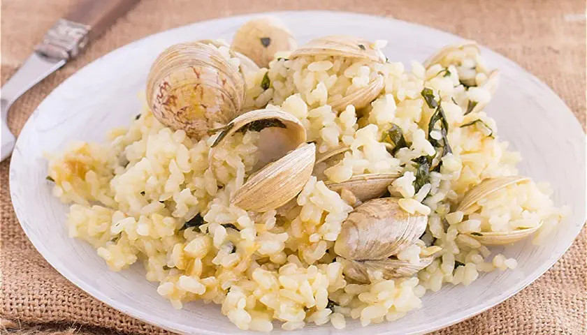 Un plato de arroz cremoso con almejas frescas, adornado con hierbas verdes. Un delicioso arroz con almejas listo para disfrutar.