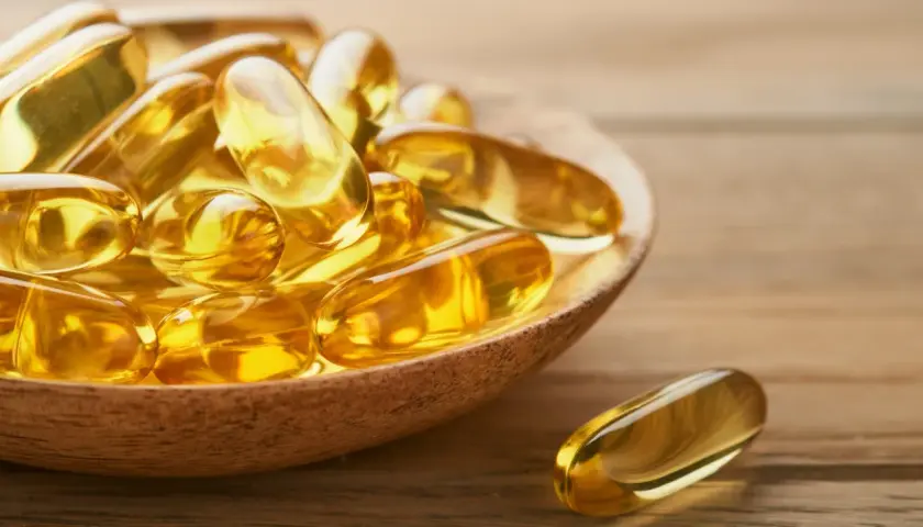 Goldene Kapseln auf einem Holzlöffel, die die positive Wirkung von Omega-3 auf die Psyche symbolisieren.