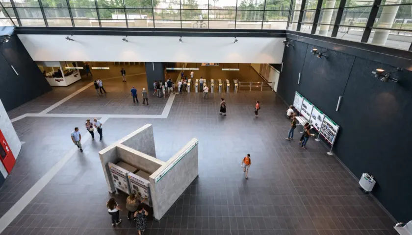 Interno moderno della fermata Teano metro C, con persone che acquistano biglietti e si dirigono verso i tornelli.
