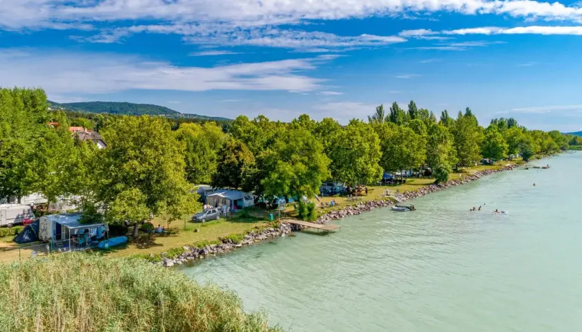 Słoneczny dzień na kempingu Balaton. Przyczepy kempingowe i namioty nad turkusową wodą, ludzie pływają i relaksują się.