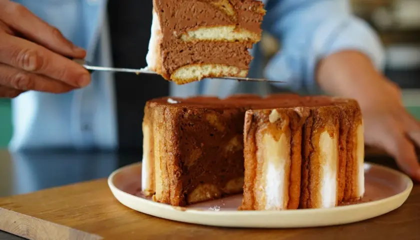 Une part de charlotte tiramisu, aérienne et chocolatée, est prélevée d'un gâteau entier.