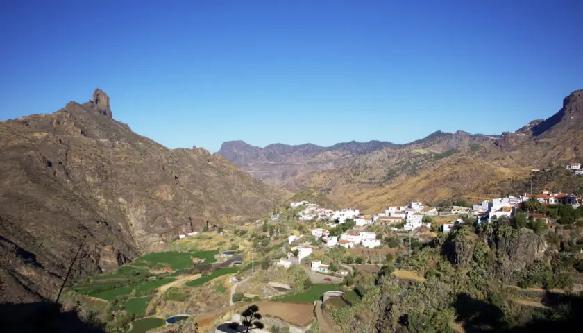 Pueblo blanco de Tejeda, Gran Canaria, con montañas escarpadas y campos verdes en un día soleado.