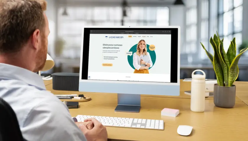Mężczyzna pracuje przy komputerze, na ekranie którego widoczna jest strona internetowa z ofertą ubezpieczeniową.