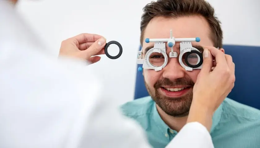Badanie wzroku u optometrysty. Mężczyzna z uśmiechem na twarzy, któremu zakładane są soczewki próbne. To pierwszy krok, by dowiedzieć się, jak zostać optometrystą.
