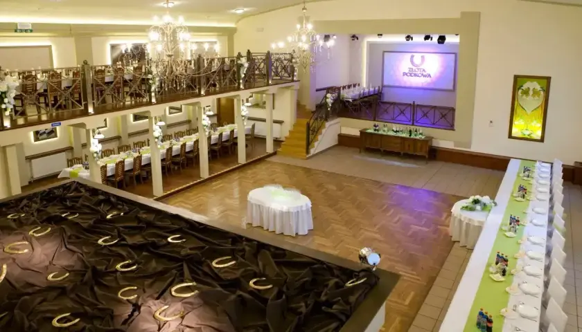 Elegancka sala weselna z podkowami na ciemnym materiale, stołami i ekranem z logo "Złota Podkowa".