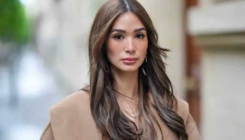 Mujer con cabello castaño largo y ondulado, viste un abrigo color camel. Su maquillaje old money resalta su belleza natural con tonos suaves y elegantes.
