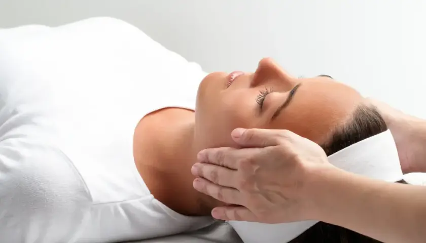 Kobieta w białej koszulce doświadcza relaksującego dotyku dłoni. To może być właśnie reiki co to za technika, która przynosi ukojenie.