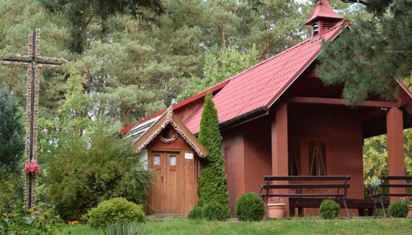 Drewniana kapliczka i krzyż ozdobiony kwiatami przy cudownym źródełku w Radoszycach.