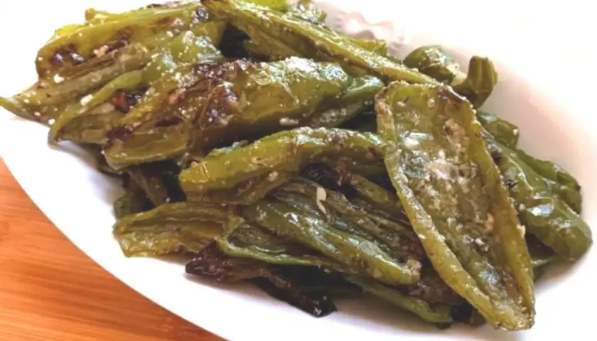 Friggitelli al forno, verdi e lucidi, conditi con sale e spezie, serviti su un piatto bianco.