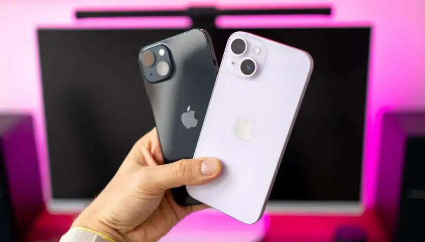 Dwa iPhone'y 14 w ręce, jeden ciemny, drugi fioletowy. Ich aparat jest gotowy do robienia zdjęć.