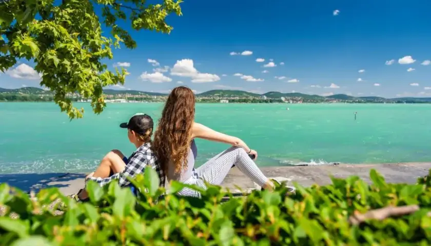 Dzieci odpoczywają na plaży Balaton, podziwiając turkusową wodę i zielone wzgórza w oddali.