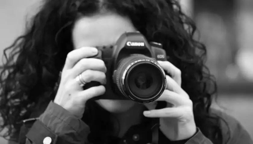 Kobieta z kręconymi włosami robi zdjęcie aparatem Canon. To jej pierwszy kurs na fotografa, uczy się łapać kadr.