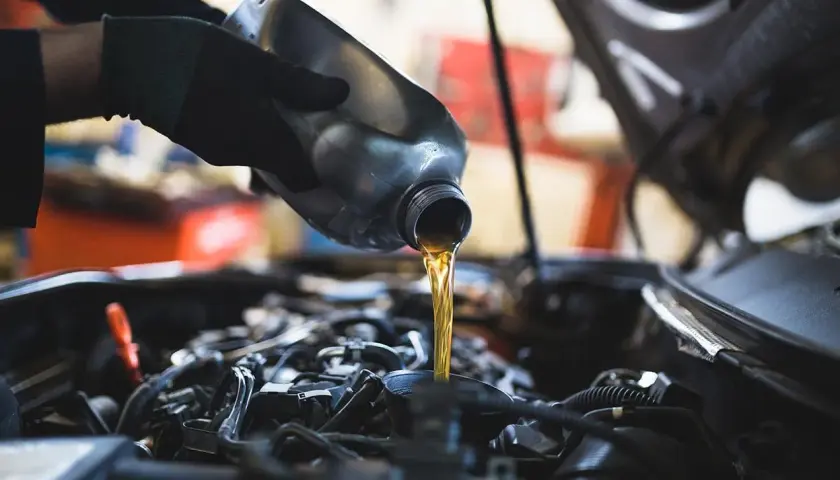 Mano con guanto versa olio motore. Un'operazione di cambio olio per un cambio manuale.