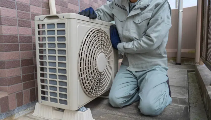 Pracownik w rękawiczkach sprawdza jednostkę zewnętrzną klimatyzacji. Wzór pozwolenia na montaż klimatyzacji w bloku jest kluczowy dla takich prac.