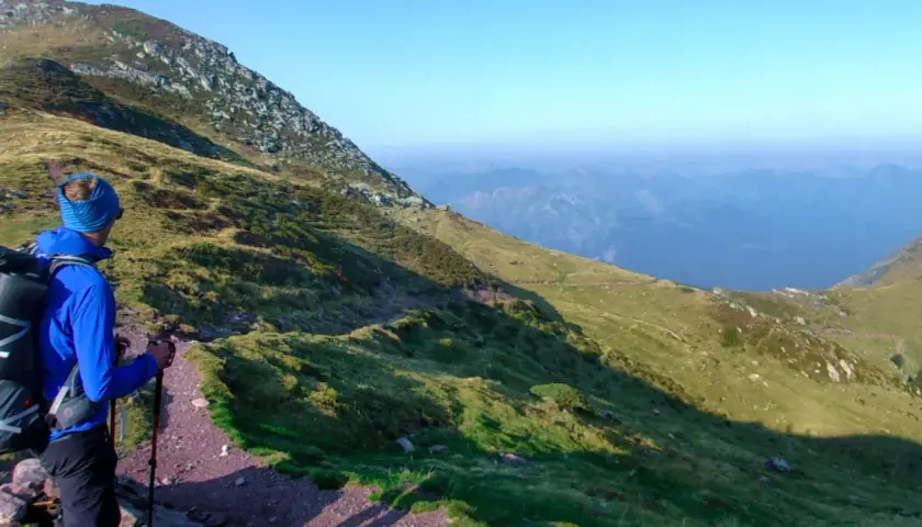 Une personne randonne seule sur un sentier de montagne, profitant d'une vue panoramique sur les vallées bleutées.